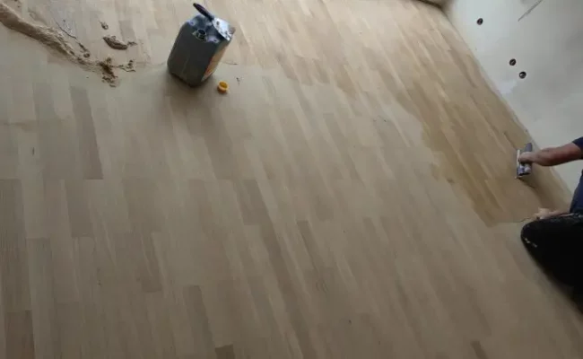 Artisan parqueteur appliquant la finition sur un parquet chêne clair — chantier 2M Parquet Net