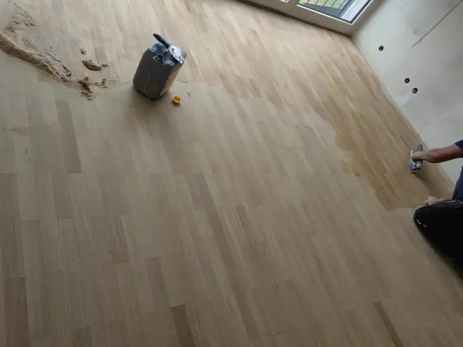Artisan parqueteur appliquant la finition sur un parquet chêne clair — chantier 2M Parquet Net